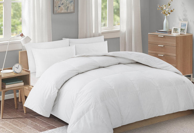 White higbedding comforter set on a wooden bed, paired with matching pillows, a bedside table, and a wooden dresser